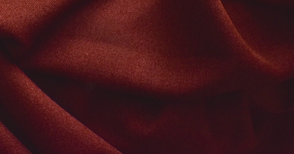 Bright lighting shining on a large piece of soft, fuzzy, burgundy fabric with wrinkles across the surface.